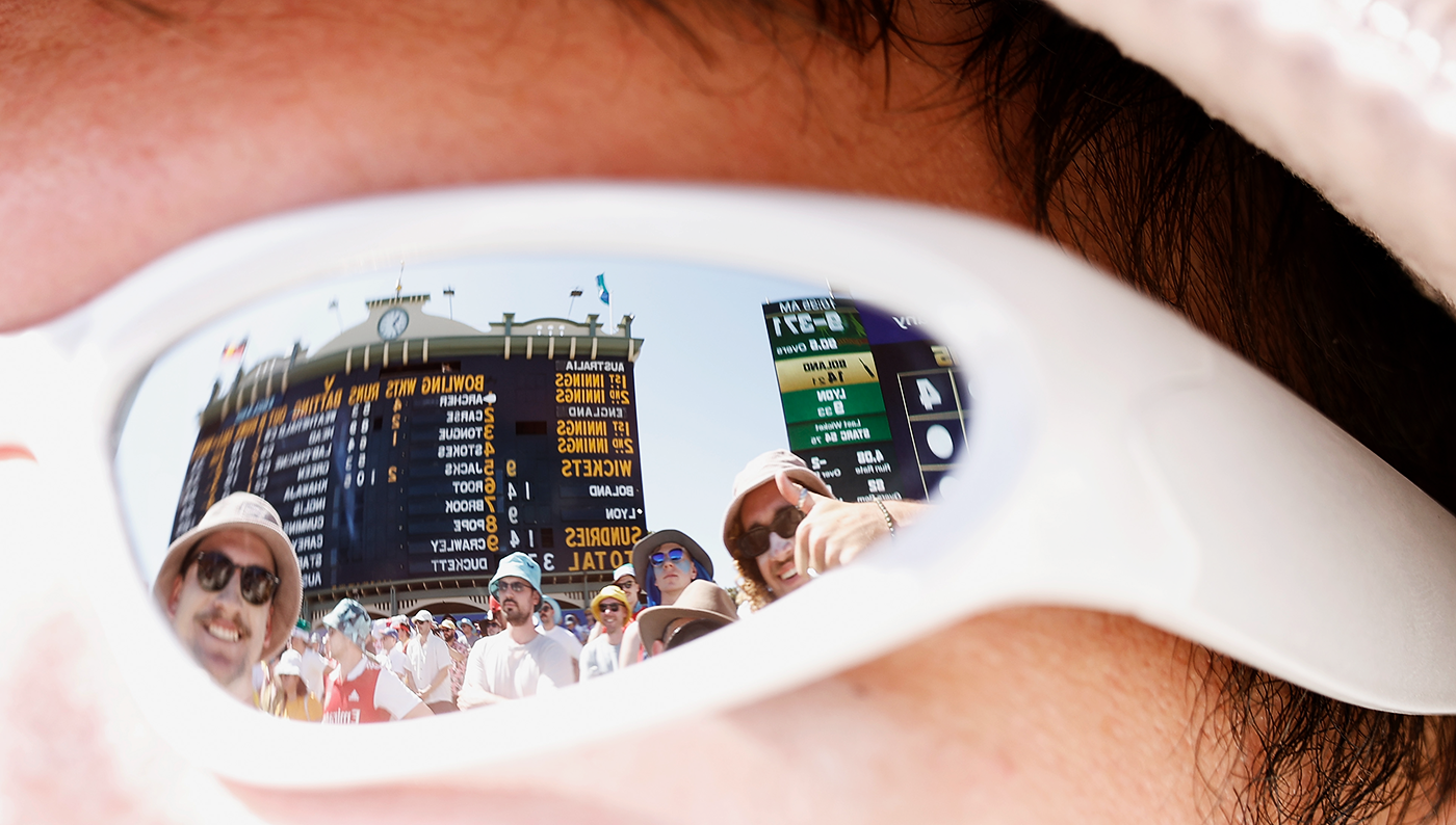 The Adelaide scoreboard and fans are reflected in the sunglasses of a spectator